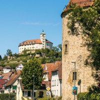 Der Pulverturm in Vaihingen an der Enz mit der Burg im Hintergrund, umgeben von Bäumen und Häusern unter blauem Himmel., © Stuttgart-Marketing GmbH, Sarah Schmid Der Pulverturm in Vaihingen an der Enz mit der Burg im Hintergrund, umgeben von Bäumen und Häusern unter blauem Himmel., © Stuttgart-Marketing GmbH, Sarah Schmid