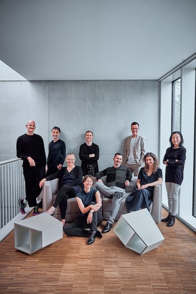 Zehn Personen posieren in einem modernen Raum mit Betonwand und Holzboden. Einige sitzen auf einem Sofa, andere stehen. Zwei geometrische Objekte liegen am Boden., © Stadt Leonberg - Amt für Kultur und Sport