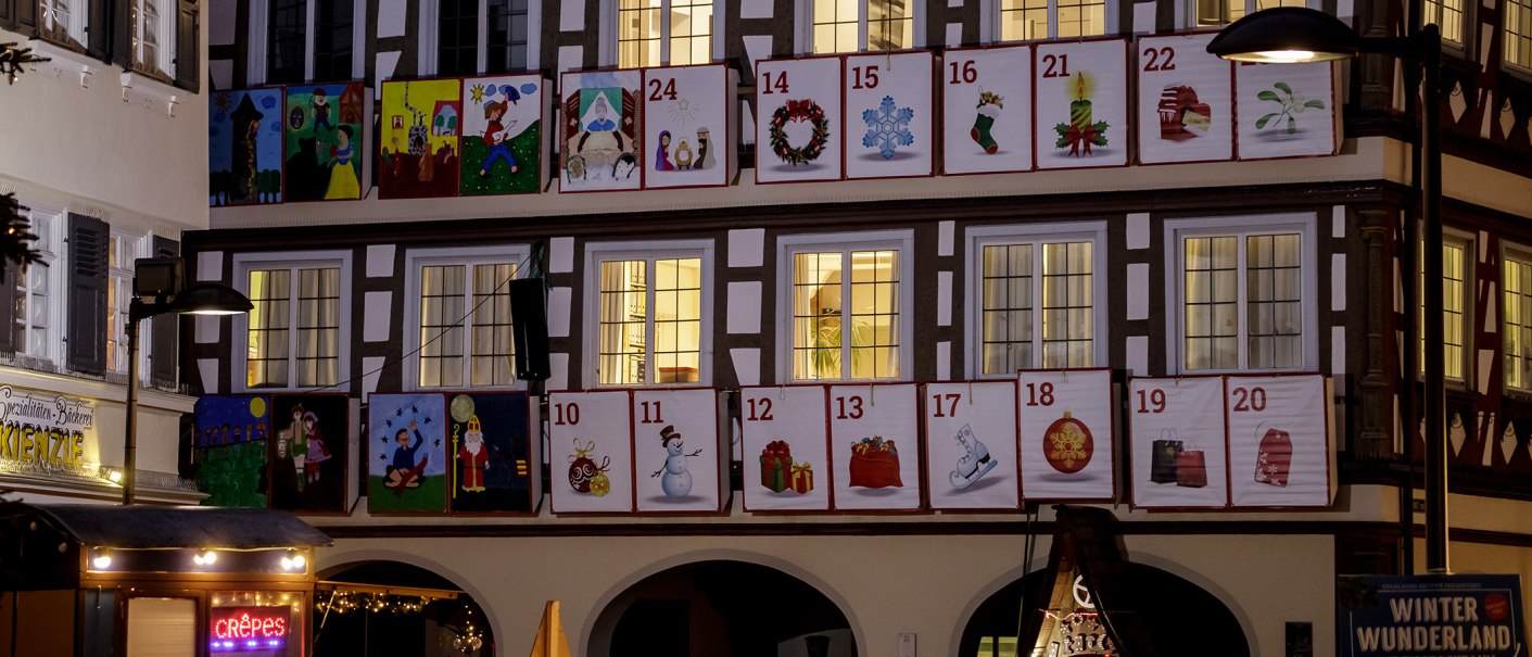 Fachwerkhaus mit Adventskalenderfenstern, nummeriert von 10 bis 24, mit weihnachtlichen Motiven. Unten ein Crêpes-Stand und ein Schild 'Winter Wunderland'., © Torsten Wenzler