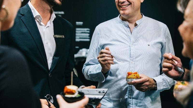 Menschen bei einem Event, die sich unterhalten und kleine Snacks genie&szlig;en. Sie wirken entspannt und fr&ouml;hlich., &copy; Mercedes-Benz AG