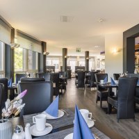 Moderner Frühstücksbereich mit gedeckten Tischen, blauen Servietten und großen Fenstern, die viel Licht hereinlassen., © Plaza INN Stuttgart-Filderstadt