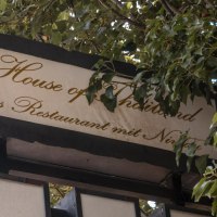 Ein Schild mit der Aufschrift 'House of Thailand, das Restaurant mit Niveau', umgeben von grünen Blättern., © Stuttgart Marketing GmbH, Sarah Schmid