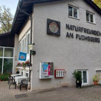 Gebäude mit der Aufschrift 'Naturfreunde am Fuchsberg', Tisch und Stühle draußen, Getränkeautomat an der Wand., © Naturfreunde Sindelfingen Gebäude mit der Aufschrift 'Naturfreunde am Fuchsberg', Tisch und Stühle draußen, Getränkeautomat an der Wand., © Naturfreunde Sindelfingen