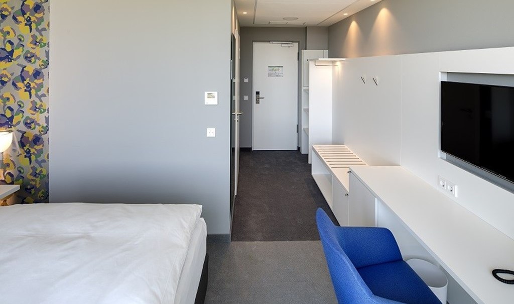 Modernes Einzelzimmer mit Bett, Schreibtisch, blauem Stuhl und Fernseher. Helle Wände und bunte Tapete an einer Seite., © Hotel am Remspark Modernes Einzelzimmer mit Bett, Schreibtisch, blauem Stuhl und Fernseher. Helle Wände und bunte Tapete an einer Seite., © Hotel am Remspark