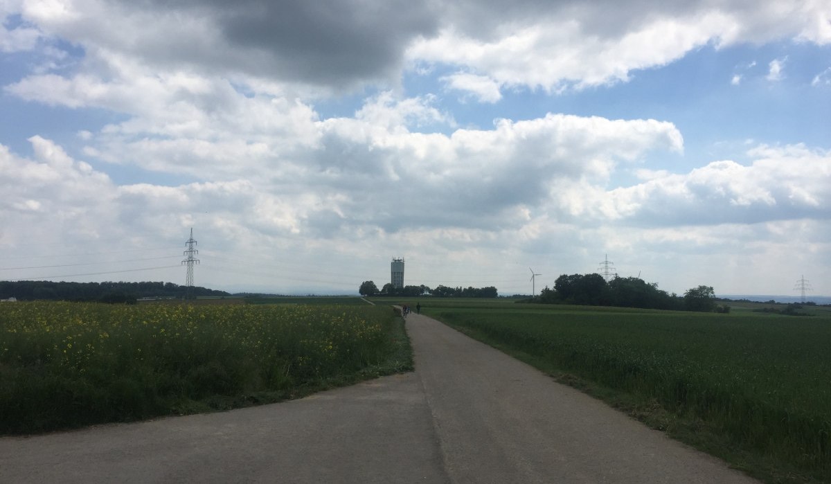 Ein Weg führt durch Felder zu einem fernen Wasserturm unter bewölktem Himmel., © www.pro-cycl.de Ein Weg führt durch Felder zu einem fernen Wasserturm unter bewölktem Himmel., © www.pro-cycl.de