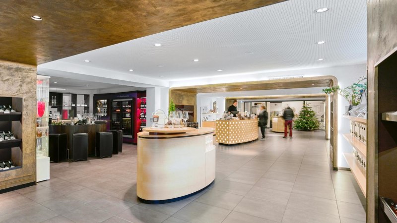 Moderne Vinothek mit eleganter Einrichtung, Weinregalen und einer zentralen Theke. Ein Weihnachtsbaum steht im Hintergrund., © Weinmanufaktur Stuttgart