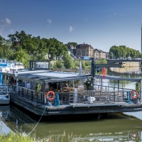 Ein schwimmendes Restaurant auf dem Neckar, umgeben von grüner Vegetation und städtischen Gebäuden im Hintergrund., © all copyrights are reserved by maks richter