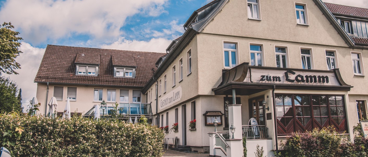 Ein traditionelles Gasthaus mit der Aufschrift 'zum Lamm', umgeben von blühenden Sträuchern und unter einem blauen Himmel mit weißen Wolken., © Stadt Welzheim