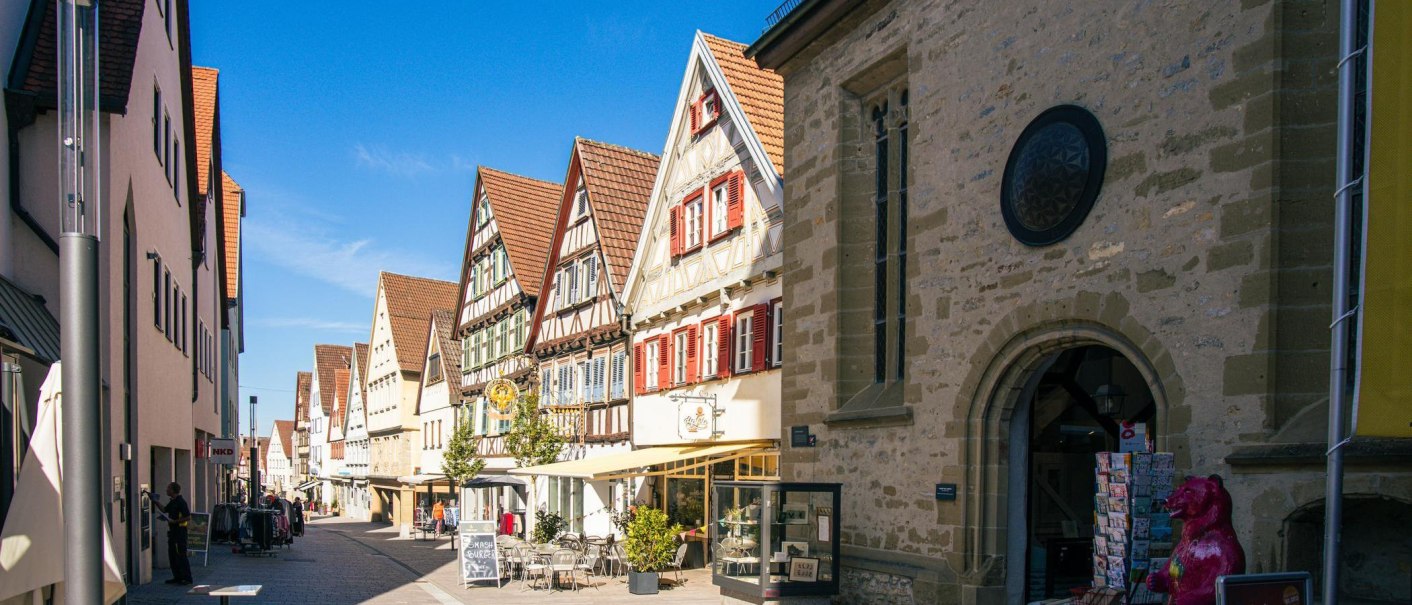 Fachwerkhäuser in der Altstadt von Marbach am Neckar. Die Straße ist belebt, mit Geschäften und Cafés. Ein sonniger Tag mit klarem Himmel., © Stuttgart-Marketing GmbH, Sarah Schmid