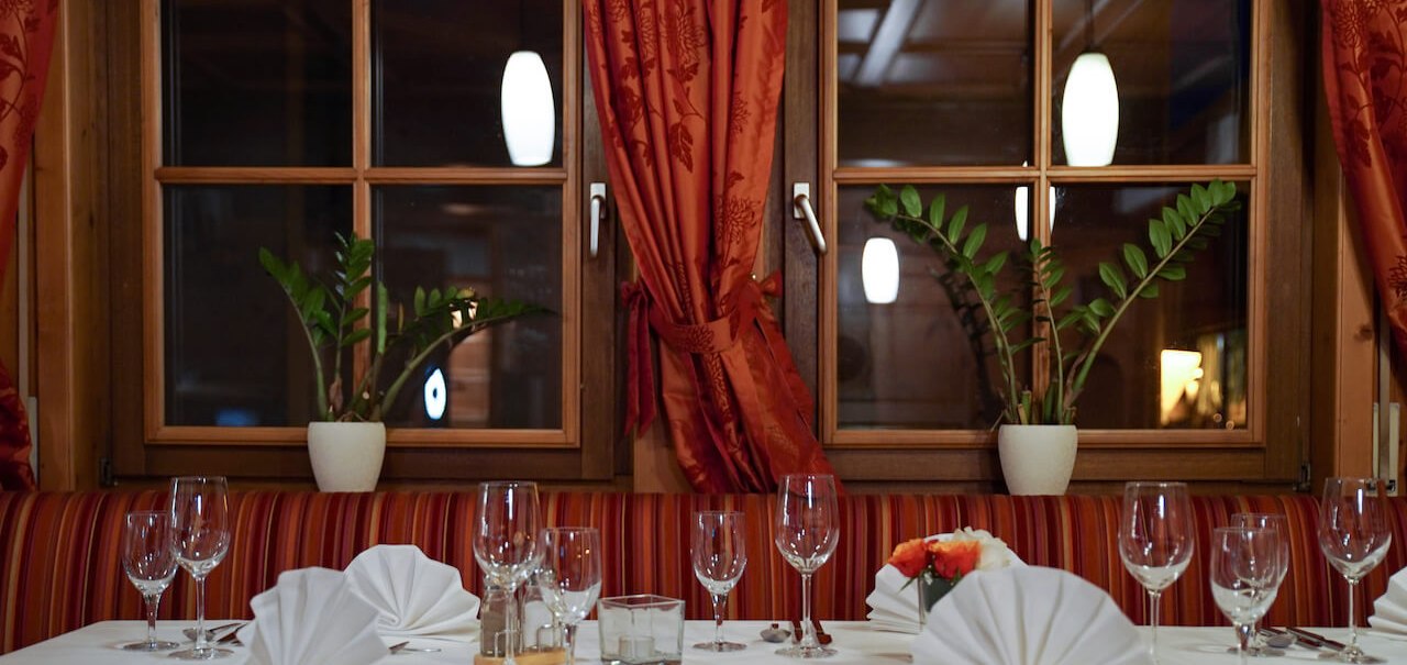 Ein stilvoll gedeckter Tisch in einem Restaurant mit weißen Tischdecken, gefalteten Servietten und Weingläsern. Im Hintergrund sind Fenster mit roten Vorhängen., © Hetzel Hotel Stuttgart Ein stilvoll gedeckter Tisch in einem Restaurant mit weißen Tischdecken, gefalteten Servietten und Weingläsern. Im Hintergrund sind Fenster mit roten Vorhängen., © Hetzel Hotel Stuttgart
