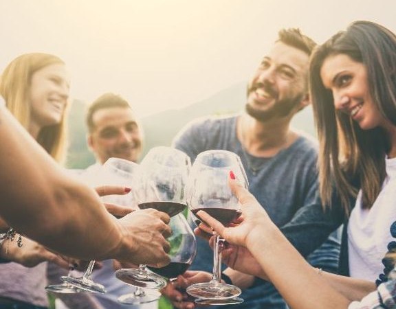 Eine Gruppe von Menschen stößt im Freien mit Weingläsern an, lächelnd und fröhlich bei sonnigem Wetter. Eine Gruppe von Menschen stößt im Freien mit Weingläsern an, lächelnd und fröhlich bei sonnigem Wetter.