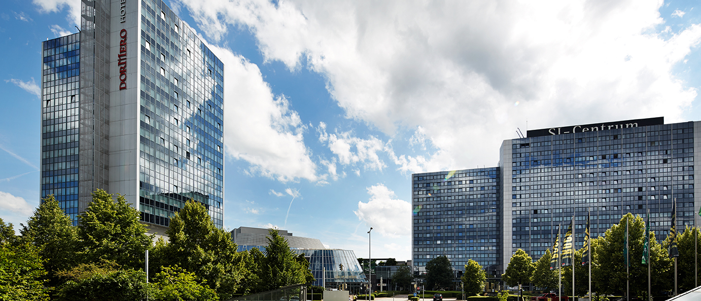 Moderne Gebäude des SI-Centrums mit Glasfassaden, umgeben von Bäumen, unter einem blauen Himmel mit Wolken., © Susanne Wegner Photography
