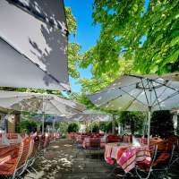 Gartenterrasse mit gedeckten Tischen unter großen Sonnenschirmen, umgeben von üppigem Grün und Bäumen., © Hotel Gasthof Hasen