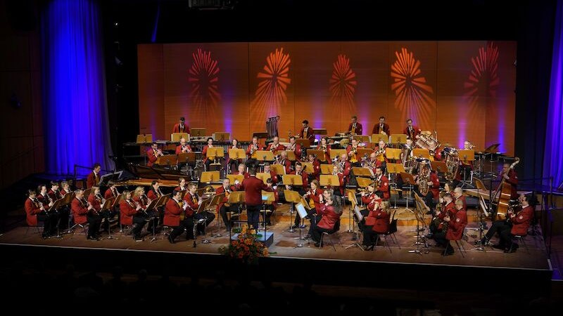 Ein Orchester in roten Uniformen spielt auf einer B&uuml;hne. Der Hintergrund ist mit bunten Lichteffekten dekoriert., &copy; Feuerwehr-Musikkapelle Dagersheim e. V.