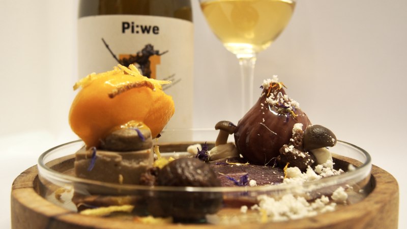 Ein kunstvoll angerichtetes Dessert mit Sorbet, Schokolade und Pilzen auf einem Holzteller. Im Hintergrund stehen eine Weinflasche und ein Glas Wei&szlig;wein., &copy; florentine N&ouml;lly