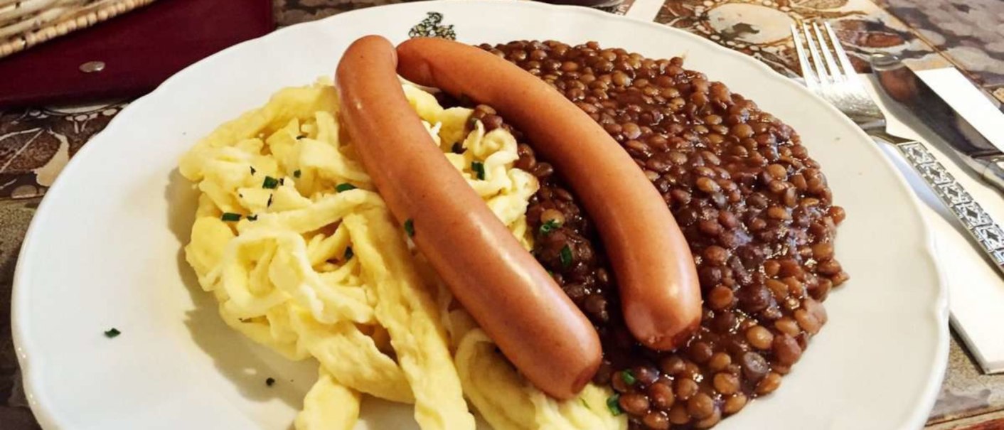 Ein Teller mit Linsen, Spätzle und zwei Würstchen, serviert auf einem Tisch mit Besteck., © TMBW, Susi Maier Ein Teller mit Linsen, Spätzle und zwei Würstchen, serviert auf einem Tisch mit Besteck., © TMBW, Susi Maier