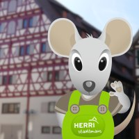 Eine animierte Maus namens Herri in grüner Latzhose steht vor einem Fachwerkgebäude. Die Maus winkt freundlich., © Stadt Herrenberg Eine animierte Maus namens Herri in grüner Latzhose steht vor einem Fachwerkgebäude. Die Maus winkt freundlich., © Stadt Herrenberg