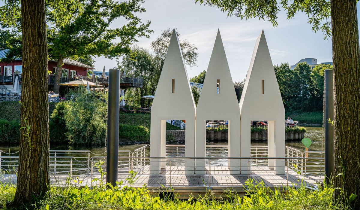 Drei weiße, spitz zulaufende Strukturen stehen am Flussufer, umgeben von Bäumen. Im Hintergrund ist ein Gebäude mit Terrasse zu sehen., © Remstal Tourismus e.V., , Architekt: Christoph Mäckler Architekten, Frankfurt Drei weiße, spitz zulaufende Strukturen stehen am Flussufer, umgeben von Bäumen. Im Hintergrund ist ein Gebäude mit Terrasse zu sehen., © Remstal Tourismus e.V., , Architekt: Christoph Mäckler Architekten, Frankfurt