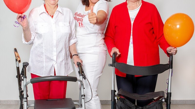 Drei Frauen feiern mit Luftballons und Partyh&uuml;ten. Zwei &auml;ltere Damen mit Rollatoren, die mittlere Frau zeigt Daumen hoch. Fr&ouml;hliche Stimmung., &copy; Mauerwerk GmbH