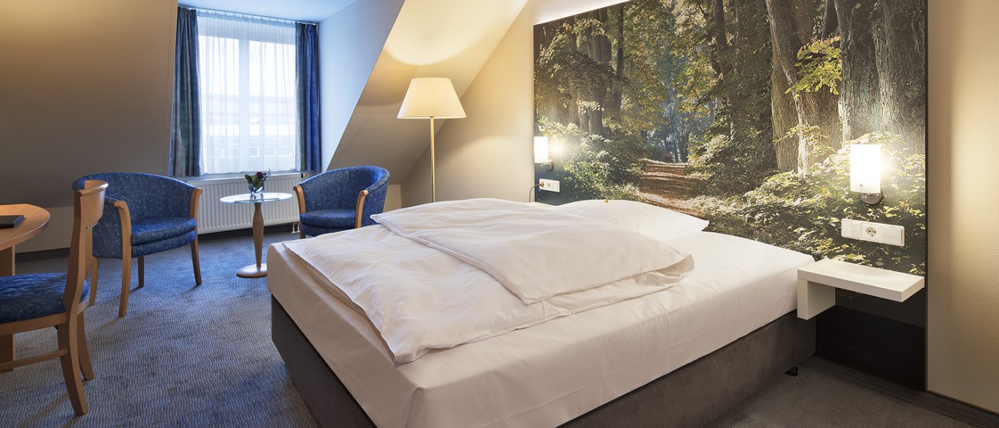 Ein stilvoll eingerichtetes Einzelzimmer mit großem Bett, blauen Sesseln und einem Tisch. Die Wand ist mit einem Waldbild dekoriert, das eine beruhigende Atmosphäre schafft., © Erikson Hotel Ein stilvoll eingerichtetes Einzelzimmer mit großem Bett, blauen Sesseln und einem Tisch. Die Wand ist mit einem Waldbild dekoriert, das eine beruhigende Atmosphäre schafft., © Erikson Hotel
