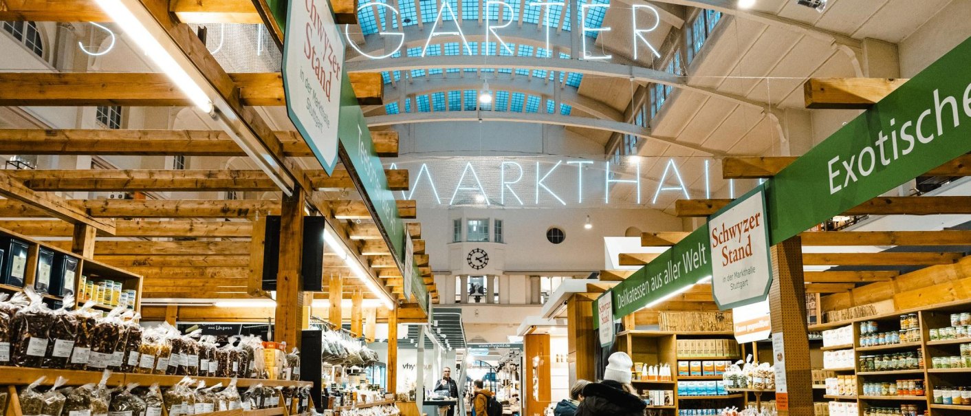 Innenansicht der Stuttgarter Markthalle mit Holzständen, Leuchtschrift und verschiedenen Verkaufsständen für Delikatessen., © Stuttgart-Marketing GmbH, Sarah Schmid