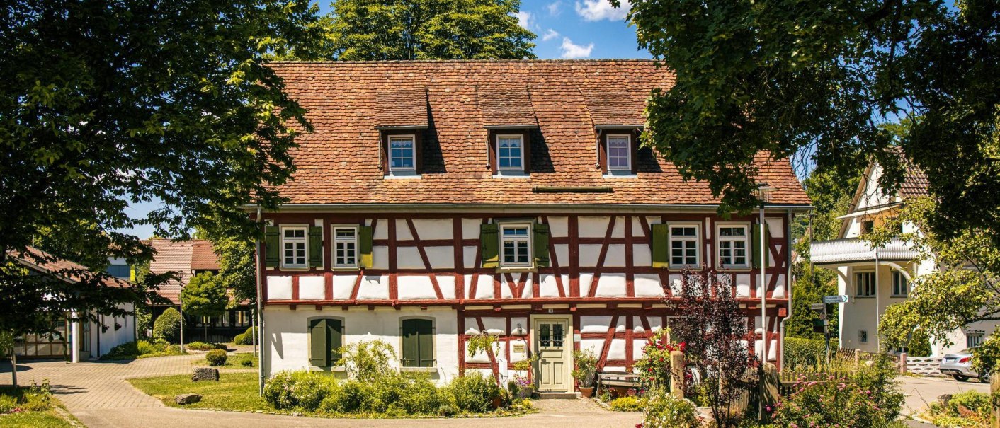 Ein traditionelles Fachwerkhaus in Murrhardt, umgeben von grünen Bäumen und einem klaren blauen Himmel. Der Garten ist gepflegt und blüht., © Stuttgart-Marketing GmbH, Sarah Schmid Ein traditionelles Fachwerkhaus in Murrhardt, umgeben von grünen Bäumen und einem klaren blauen Himmel. Der Garten ist gepflegt und blüht., © Stuttgart-Marketing GmbH, Sarah Schmid