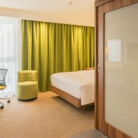 Modernes Hotelzimmer mit Doppelbett, grünem Sessel, Schreibtisch und Blick ins Badezimmer mit Dusche. Helle Vorhänge und grüne Gardinen., © Hampton by Hilton Stuttgart City Centre Modernes Hotelzimmer mit Doppelbett, grünem Sessel, Schreibtisch und Blick ins Badezimmer mit Dusche. Helle Vorhänge und grüne Gardinen., © Hampton by Hilton Stuttgart City Centre