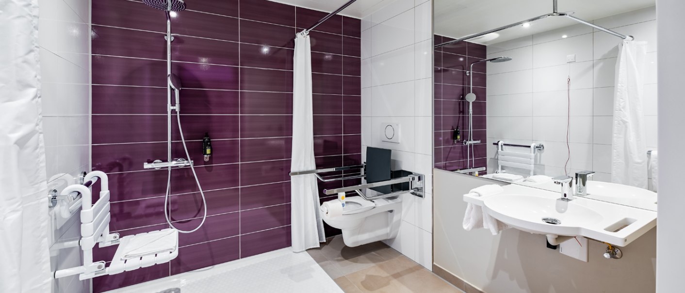 Modernes, behindertengerechtes Badezimmer mit lila Fliesen, Haltegriffen, Duschsitz, WC und Waschbecken. Barrierefreie Ausstattung., © Premier Inn
