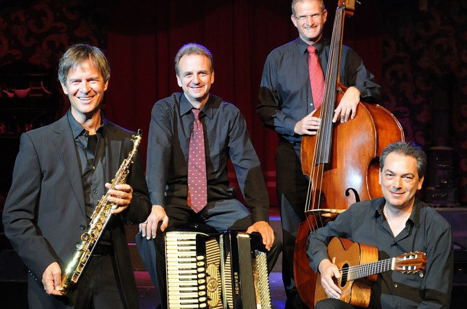 Eine Jazzband mit Saxophon, Akkordeon, Kontrabass und Gitarre posiert auf einer Bühne. Die Musiker tragen dunkle Anzüge und lächeln in die Kamera., © Stadt Murrhardt Eine Jazzband mit Saxophon, Akkordeon, Kontrabass und Gitarre posiert auf einer Bühne. Die Musiker tragen dunkle Anzüge und lächeln in die Kamera., © Stadt Murrhardt