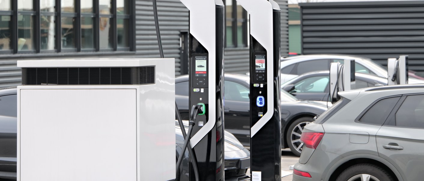 Zwei moderne Elektroladestationen auf einem Parkplatz, umgeben von geparkten Autos. Im Hintergrund ein Gebäude mit großen Fenstern., © V8 HOTEL Motorworld Region Stuttgart Zwei moderne Elektroladestationen auf einem Parkplatz, umgeben von geparkten Autos. Im Hintergrund ein Gebäude mit großen Fenstern., © V8 HOTEL Motorworld Region Stuttgart