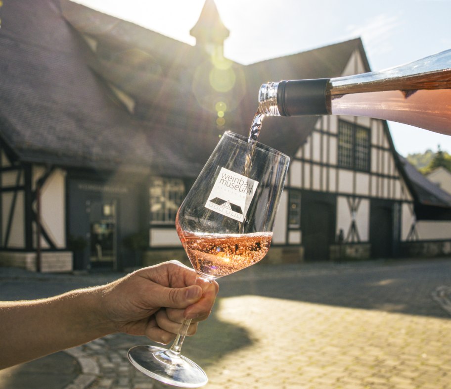 Ros&eacute;wein wird vor dem Weinbaumuseum in ein Glas eingeschenkt, im Hintergrund ein Fachwerkgeb&auml;ude im Sonnenlicht., &copy; SMG, Sarah Schmid