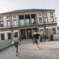 Das StadtPalais Stuttgart mit klassischer Fassade, Menschen gehen auf einem gepflasterten Weg davor. Im Hintergrund sind Bäume und ein sonniger Himmel., © Stuttgart-Marketing GmbH, WP Steinheisser