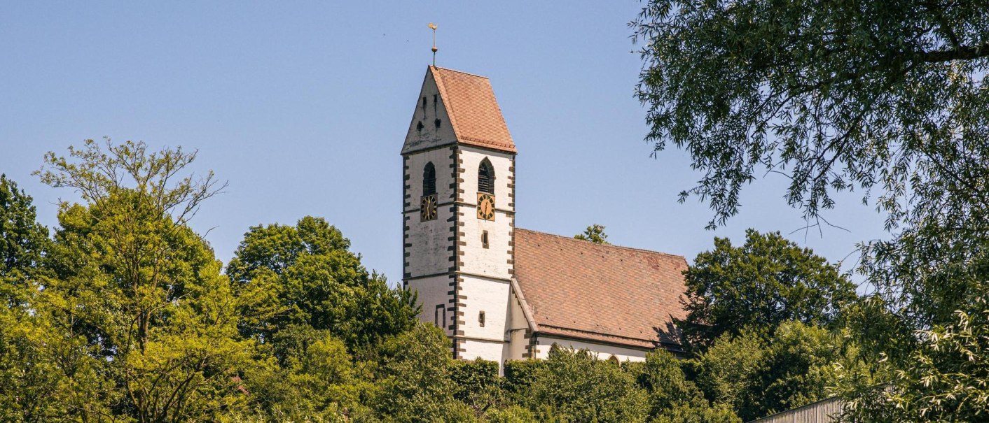 Die St. Blasius Kirche in Plochingen erhebt sich majest&auml;tisch &uuml;ber die umgebenden B&auml;ume, mit ihrem markanten Turm und dem blauen Himmel im Hintergrund., &copy; Stuttgart-Marketing GmbH, Sarah Schmid