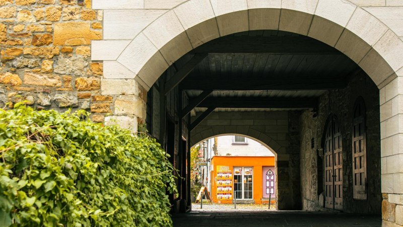 Ein steinerner Torbogen f&uuml;hrt zu einem orangefarbenen Geb&auml;ude. Links sind gr&uuml;ne Pflanzen, rechts eine Steinmauer., &copy; Stuttgart-Marketing GmbH, Sarah Schmid
