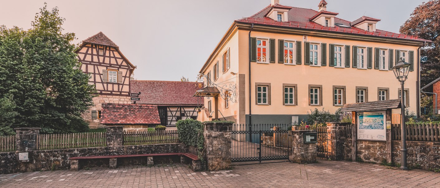 Ein historisches Fachwerkhaus neben einem modernen Gebäude mit grünen Fensterläden in Welzheim. Davor ein gepflasterter Platz und ein schmiedeeisernes Tor., © Stadt Welzheim Ein historisches Fachwerkhaus neben einem modernen Gebäude mit grünen Fensterläden in Welzheim. Davor ein gepflasterter Platz und ein schmiedeeisernes Tor., © Stadt Welzheim