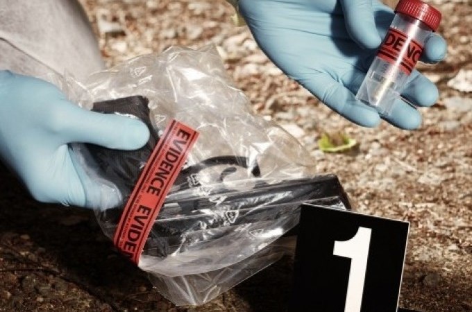 Tatortszene mit Beweismitteln: Eine Pistole in einer Tüte und ein Probenröhrchen werden von behandschuhten Händen untersucht, markiert mit Nummer 1., © Cool-Tours StattReisen Tatortszene mit Beweismitteln: Eine Pistole in einer Tüte und ein Probenröhrchen werden von behandschuhten Händen untersucht, markiert mit Nummer 1., © Cool-Tours StattReisen