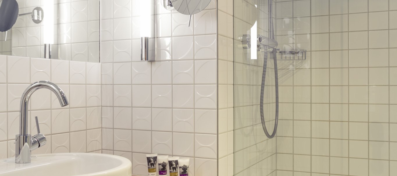 Modernes Badezimmer mit weiß gefliesten Wänden, rundem Waschbecken, Spiegel, Handtüchern und einer Glasduschkabine., © Mercure Bristol Stuttgart Sindelfingen