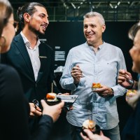 Menschen in formeller Kleidung unterhalten sich bei einem Empfang und genießen kleine Häppchen. Sie wirken fröhlich und entspannt., © Mercedes-Benz AG