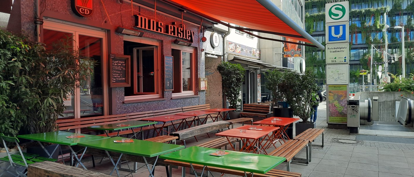 Außenbereich eines Cafés namens Mos Eisley mit bunten Tischen und Bänken. Daneben ein S- und U-Bahn-Schild am Rotebühlplatz Stadtmitte., © SMG