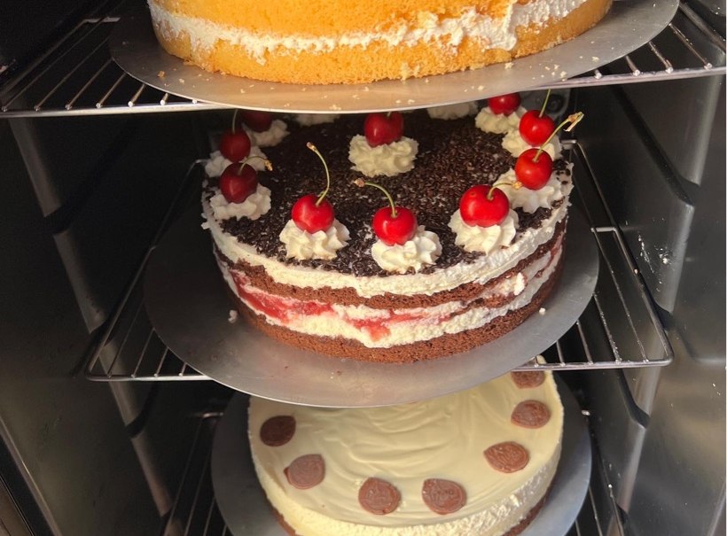 Vier verschiedene Kuchen in einem Kühlschrank gestapelt, darunter eine Schwarzwälder Kirschtorte und ein Kuchen mit Mandeln., © Café Plätschwiesle
