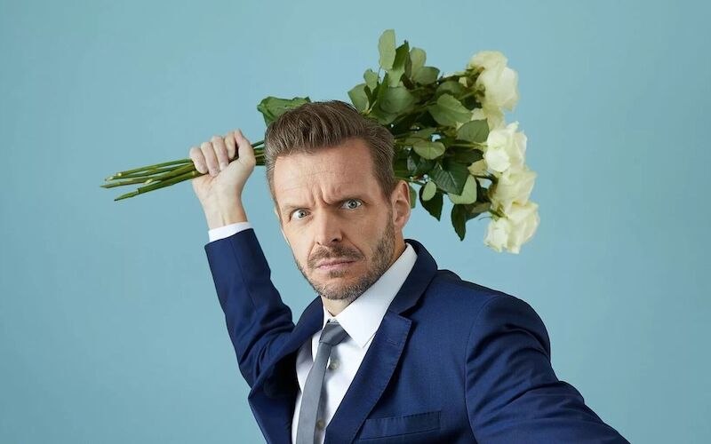 Ein Mann in einem blauen Anzug posiert dramatisch mit einem Strau&szlig; wei&szlig;er Rosen vor einem blauen Hintergrund., &copy; Konzertkreis Triangel Compagnia Compostelli e.V.