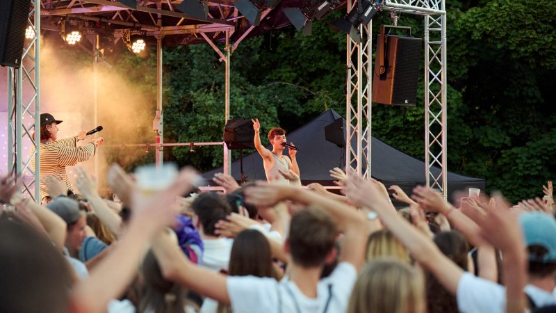 Ein S&auml;nger performt auf einer Open-Air-B&uuml;hne vor einem jubelnden Publikum. Die Zuschauer heben die H&auml;nde in die Luft, w&auml;hrend der K&uuml;nstler singt., &copy; www.peter-oppenlaender.de
