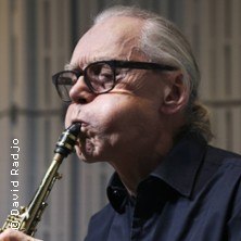 Ein älterer Mann mit Brille spielt konzentriert Saxophon. Er trägt ein dunkles Hemd und hat graue Haare., © links im Bild Ein älterer Mann mit Brille spielt konzentriert Saxophon. Er trägt ein dunkles Hemd und hat graue Haare., © links im Bild
