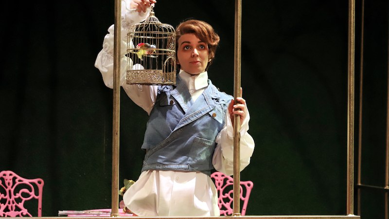 Person in historischem Kostüm hält einen Vogelkäfig. Im Hintergrund sind rosa Stühle zu sehen. Szene aus einer Theateraufführung., © Kulturbüro Schwäbisch Gmünd