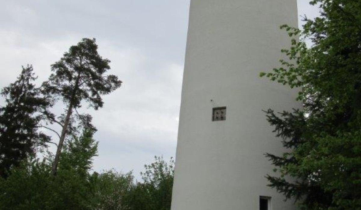 Ein weißer, runder Wasserturm in Jettingen steht vor einem bewölkten Himmel, umgeben von Bäumen und einer Bank mit Gießkanne., © Natur.Nah. Schönbuch & Heckengäu Ein weißer, runder Wasserturm in Jettingen steht vor einem bewölkten Himmel, umgeben von Bäumen und einer Bank mit Gießkanne., © Natur.Nah. Schönbuch & Heckengäu
