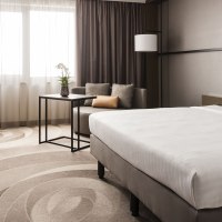 Modernes Hotelzimmer mit gro&szlig;em Bett, Sofa, Tisch und Fernseher. Helle Vorh&auml;nge und dezente Farben schaffen eine elegante Atmosph&auml;re., &copy; Stuttgart Marriott Hotel Sindelfingen