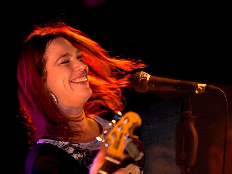 Eine Frau mit roten Haaren singt lächelnd in ein Mikrofon und spielt Gitarre auf der Bühne., © Stadt Sindelfingen Eine Frau mit roten Haaren singt lächelnd in ein Mikrofon und spielt Gitarre auf der Bühne., © Stadt Sindelfingen