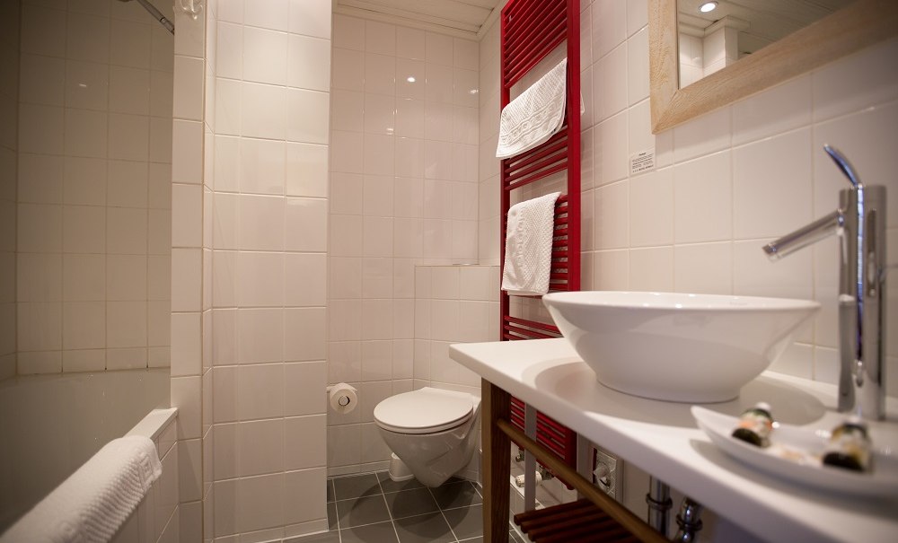 Modernes Badezimmer mit wei&szlig;er Keramik, rotem Handtuchheizk&ouml;rper und gro&szlig;er Spiegel. Die W&auml;nde sind gefliest, der Boden ist grau., &copy; Hotel B&uuml;rkle
