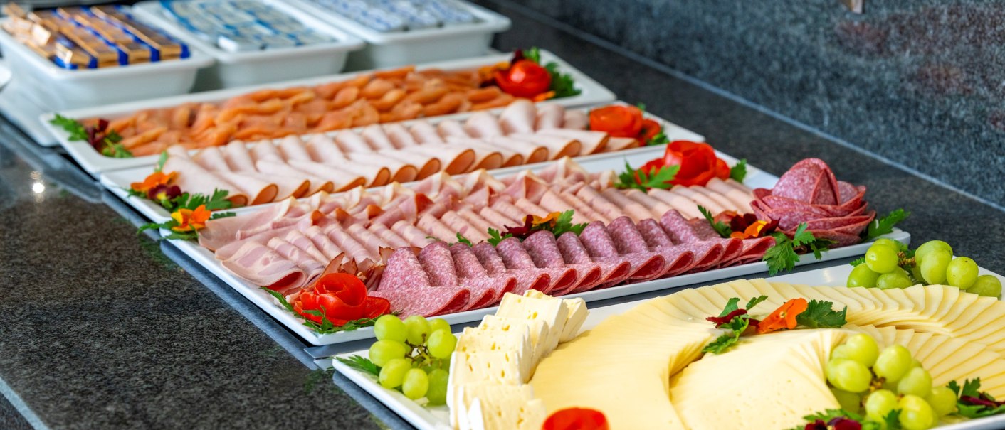 Ein reichhaltiges Frühstücksbuffet mit Wurst- und Käsesorten, dekoriert mit Trauben und Tomaten auf weißen Platten., © Plaza Residence Stuttgart-Ditzingen Ein reichhaltiges Frühstücksbuffet mit Wurst- und Käsesorten, dekoriert mit Trauben und Tomaten auf weißen Platten., © Plaza Residence Stuttgart-Ditzingen