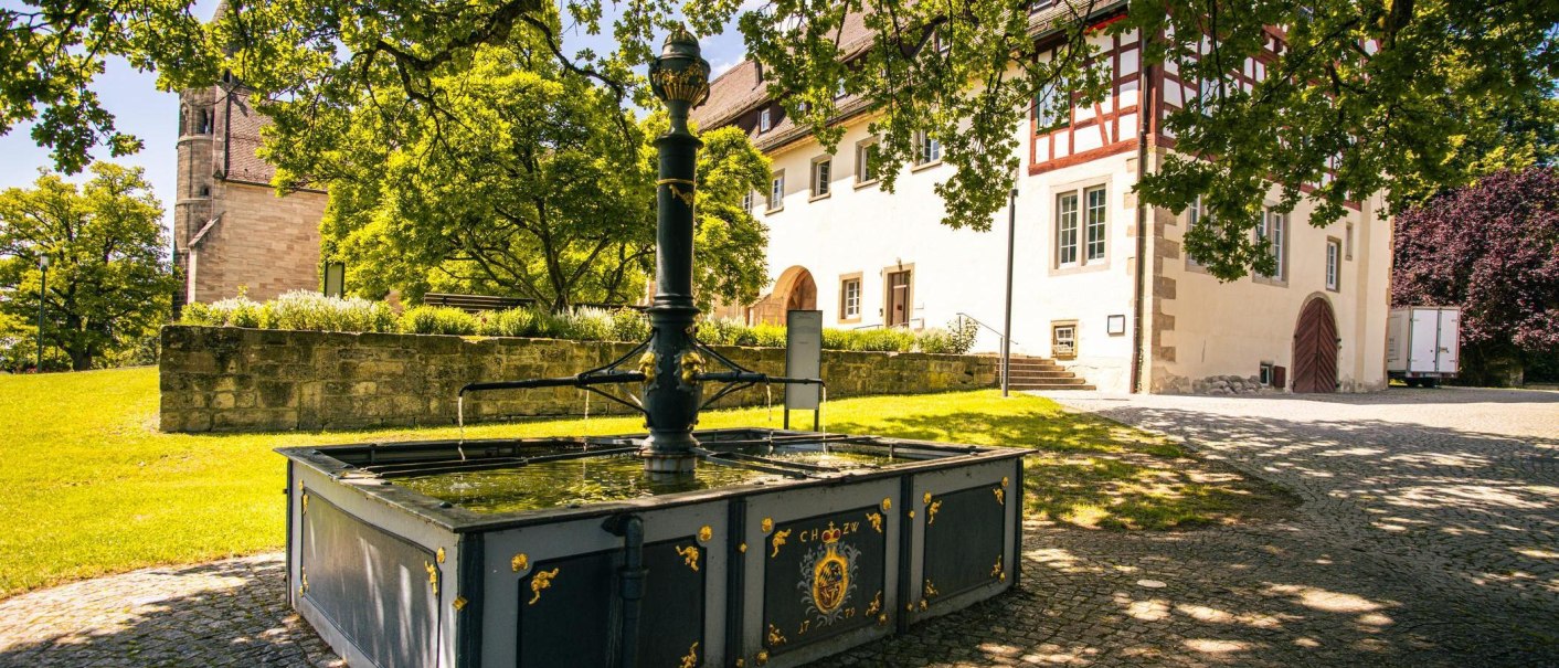 Ein Brunnen im Vordergrund vor dem Kloster Lorch, umgeben von Bäumen und einem gepflegten Rasen. Historische Architektur im Hintergrund., © Stuttgart-Marketing GmbH, Sarah Schmid Ein Brunnen im Vordergrund vor dem Kloster Lorch, umgeben von Bäumen und einem gepflegten Rasen. Historische Architektur im Hintergrund., © Stuttgart-Marketing GmbH, Sarah Schmid